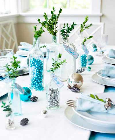 Table decorated with bottles filled with bells and Christmas green.